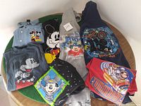 Top-down view of all seven Disney hoodies and shirts arranged in a circle showing various designs and colors.