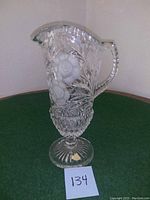 Front side view of large hand cut crystal pitcher vase, showing floral and leaf patterns.