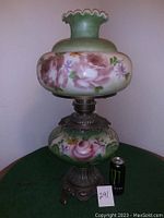 Overall view of the vintage hand-painted hurricane lamp with floral designs, decorative metal base, and ruffled green glass top.