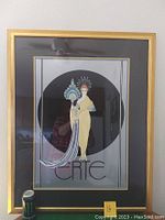 Full view of framed Erté print showing stylized female figure with elaborate headdress and fan in gold frame with black and gold matting.