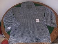 Front view of the chainmail shirt spread out on a round table showing full length sleeved armor and neck guard.