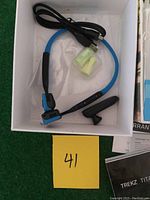 Photo of Trekz Titanium headphones, USB charger cable, and earplugs in the box against a green background with lot card #41