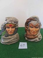 Front view of two ceramic candle holders shaped as female busts with animal headpieces.