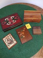 Top view of the set of five vintage decorative boxes with various designs and sizes on a wooden surface covered with green cloth.