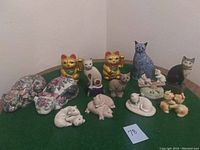 Overview of the full collection of vintage cats and pigs figurines laid out on a green surface, showing various sizes and styles.