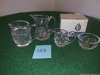 Four Waterford Crystal pieces displayed on green surface: sugar bowl with lid, creamer pitcher, small pitcher, small bowl alongside original box.