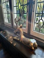 Full view of brass deer figurine placed by leaded window