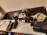 Wide view of Canon camera body with attached grip, Canon EF 70-210mm lens, flash, camera straps, and assorted accessories spread on a cloth surface.