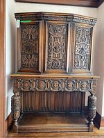 Front view of antique carved oak buffet and hutch showing three ornately carved door panels on hutch and carved apron on buffet base with turned legs.