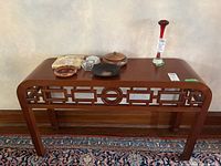 Full view of the wood Chinese style hall table with a decorative lattice apron and items placed on top.