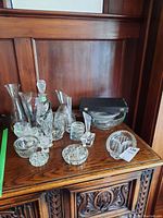Table showing multiple crystal decanters, pitchers, shot glasses, and small plates arranged on a wooden surface.