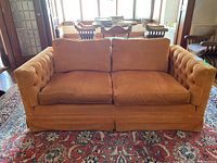 Front view of mustard orange velvet loveseat showing two loose seat and back cushions, tufted arms and pleated skirt