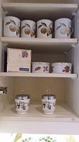 Four ceramic mugs with fruit designs on a shelf
