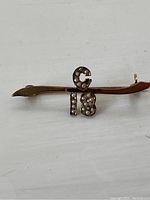 Close-up front view of the antique gold pin with seed pearls forming the characters 'G 18'. One seed pearl is missing from the letter 'G'.