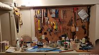 Wide view of pegboard with hanging hand tools like saws, hammer, brushes, levels, and various small items set on a table below.