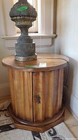 Side view of the round wood side table showing vertical ribbed wooden panel cabinet base and single door with keyhole.
