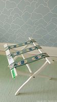 Side angle view of the white wooden folding stand showing the green fabric straps with floral patterns and crossed legs.