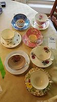 Photo showing all seven teacups and saucers arranged on a table with distinct floral patterns and colors.