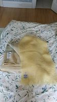 Three blankets and wraps on floral bedspread: yellow mohair wrap, cream Glen Cree mohair wool blanket with green stripes, partially visible Rosslyn blanket underneath.