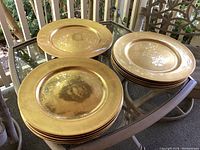 12 gold marbled chargers, 13 inches diameter each, stacked with 1 larger 14 inch charger on a glass table.