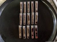 15 high quality metal nail clippers arranged in rows on a black tray, showing the top lever side with brand name and markings visible.