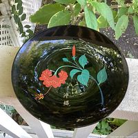 Top view of the black lacquer plate showing the red hibiscus flower, green leaves, red flower bud, and gold Japanese markings.