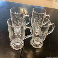 Four Princess House vintage crystal glasses on dark wooden table, showing etched floral pattern and pedestal bases from top-front angle.