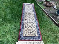 Full view of the full length of the beige and navy blue runner rug laid out on grass, showing overall size and pattern.