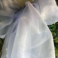 Light blue sheer scarf tied in a large bow, fabric is translucent and flowing, shown against outdoor background.