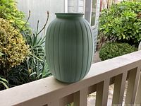 Side view of the mint green vintage vase with vertical ribbing sitting on a porch railing.