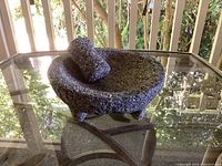 Side angle view of the three-legged, roughly textured granite mortar on a glass table.