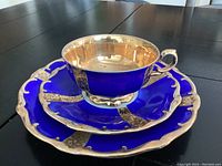 Photo showing the tea cup placed upside down on the plates, displaying the gold plated interior of the tea cup along with the deep cobalt blue and gold plated ornate edges of the saucer and plate underneath.