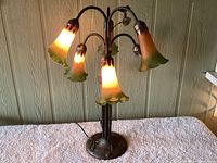 Full front view of six tulip lamp lit with warm amber-green glass shades on metal base.
