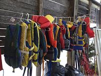 Wide shot of 11 assorted life jackets hanging on a rod, showing various colors and sizes.