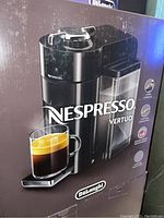 Photo of the Nespresso Vertuo coffee maker in its original box, showing the machine and brand logos.