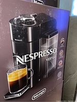 Front view of the Nespresso Vertuo box showing coffee maker and a glass cup of black coffee with crema.