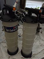 Two cylindrical plastic oil extractors side by side, showing their overall shape, sizes and handles.