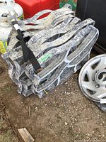 Strapped stack of gray plastic sidewalk molds on ground next to hubcaps and propane tanks