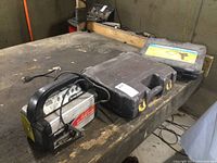 Full lot showing Power On Demand battery charger, two black plastic cases, one likely containing the Ryobi drill, and smaller case likely the inspection camera.