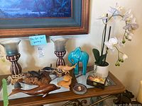 Wide view of the entire lot showing candle sticks, wood and ceramic animal figurines, faux orchid, trinket box, and dish on a glass surface
