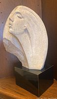 Side view of a textured beige sculptural bust of a woman on black base