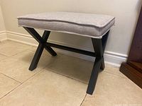 Side angle of the bench seat showing the black X-frame legs and the cushioned fabric seat.