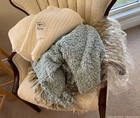Three lightweight blankets placed on an upholstered chair, showing various textures and tassel features.