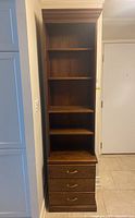 Front view showing tall wood veneer bookcase with three drawers and shelves.
