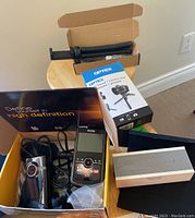 Overview of lot items including Kodak Zi8 camera, Flip MinoHD camera, cables, Jambox Bluetooth speaker, and two tripods on a stool and box