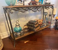 Console table in front of wall showing metal frame with scroll design and items placed on glass lower shelf.
