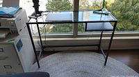 Desk positioned in front of window showing metal frame and glass surface.