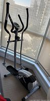 Full side and front view of the elliptical showing pedal, frame, and handles near a window.