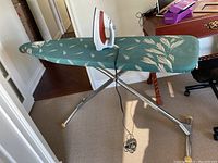Ironing board set up with iron on top, showing full board and metal legs with rubber foot grips