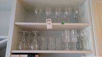 Wide cabinet shot showing all crystal glassware in set: wine glasses, champagne flutes, tumblers, and old fashioned glasses.